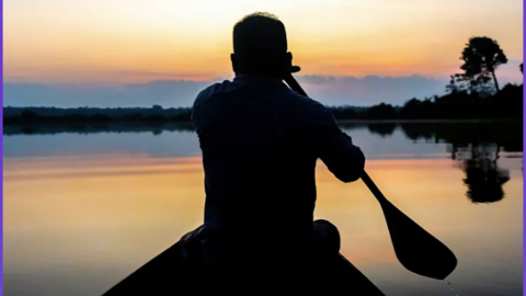 Man rowing in the water during a sunset