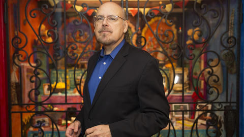 David Carrasco wearing glasses and a suit standing in front of a Day of the Dead altar at the Peabody Museum of Archaeology & Ethnology. Photo by Kris Snibbe/Harvard University.