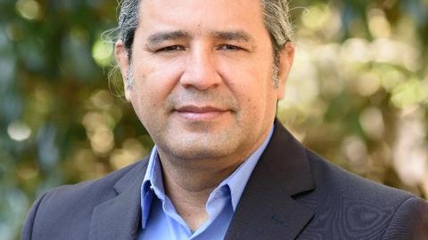 A professional headshot of Indigenous Radcliffe Fellow Emil' Keme in a blue suit