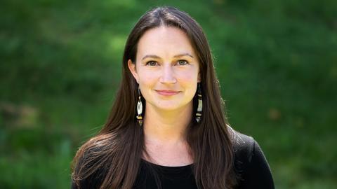 A photo of Rachel Wilbur in a black shirt in front of a blurred green background