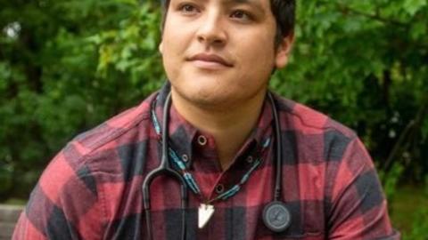 Victor Lopez-Carmen in a red and black flannel with a stethoscope hung around his neck